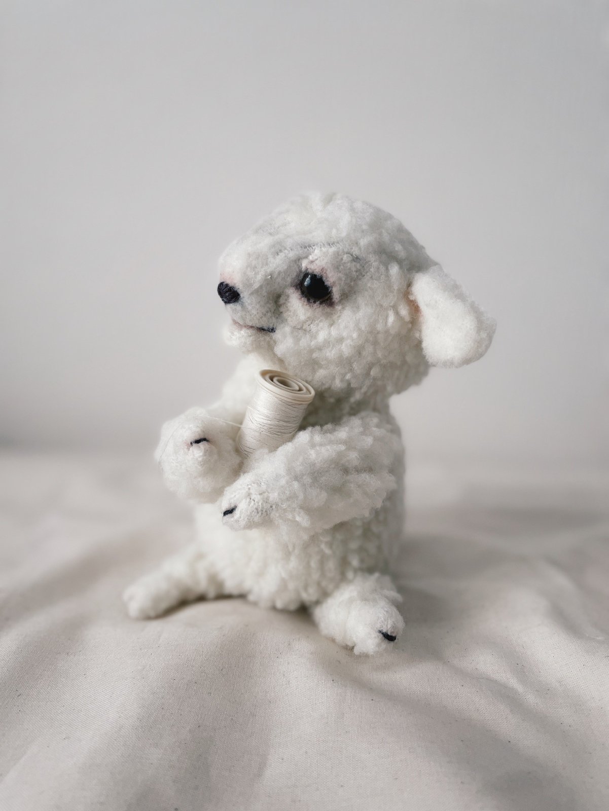巻かれた糸を持って横を向くひつじのぬいぐるみ